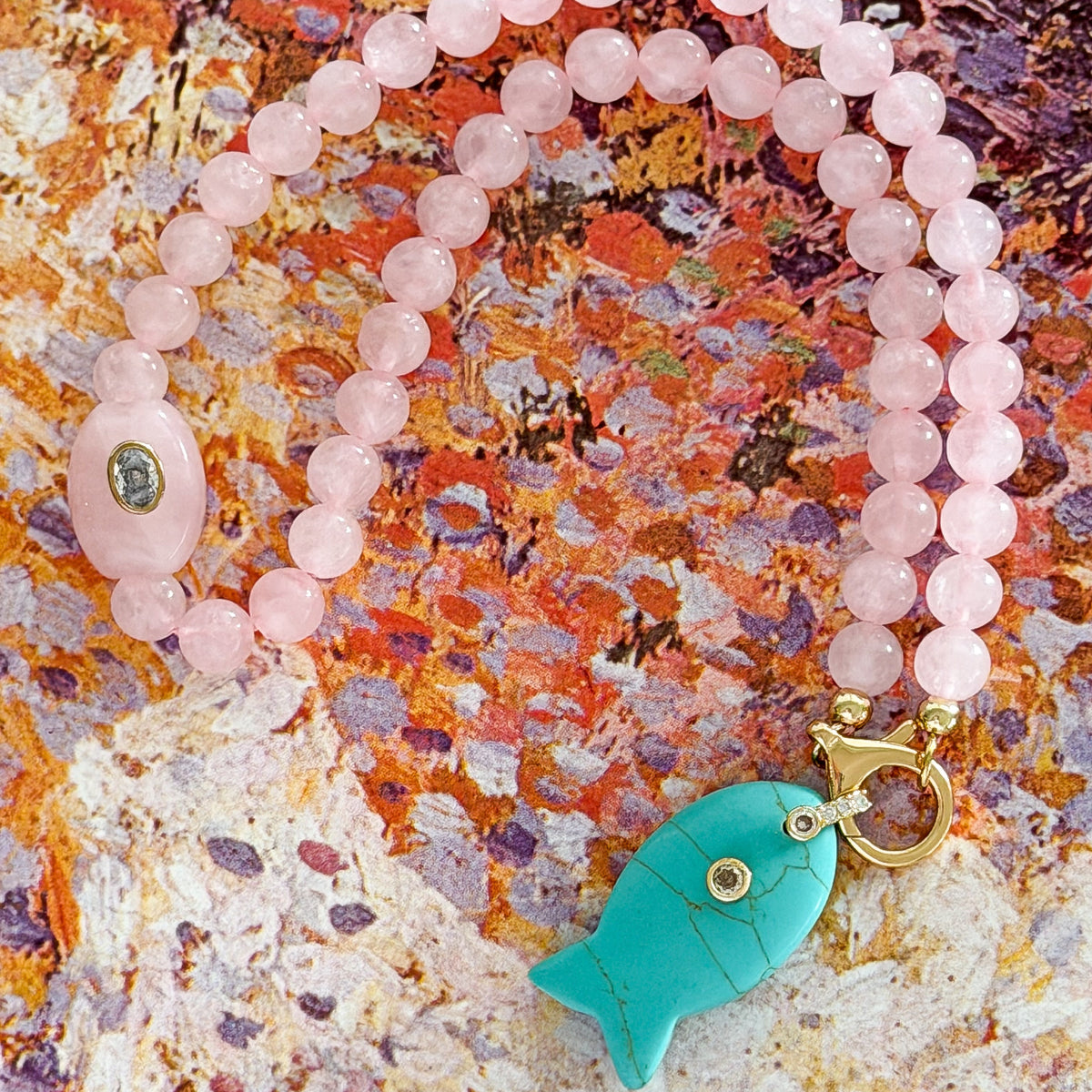Necklace with pink beads and a turquoise fish pendant on a textured surface