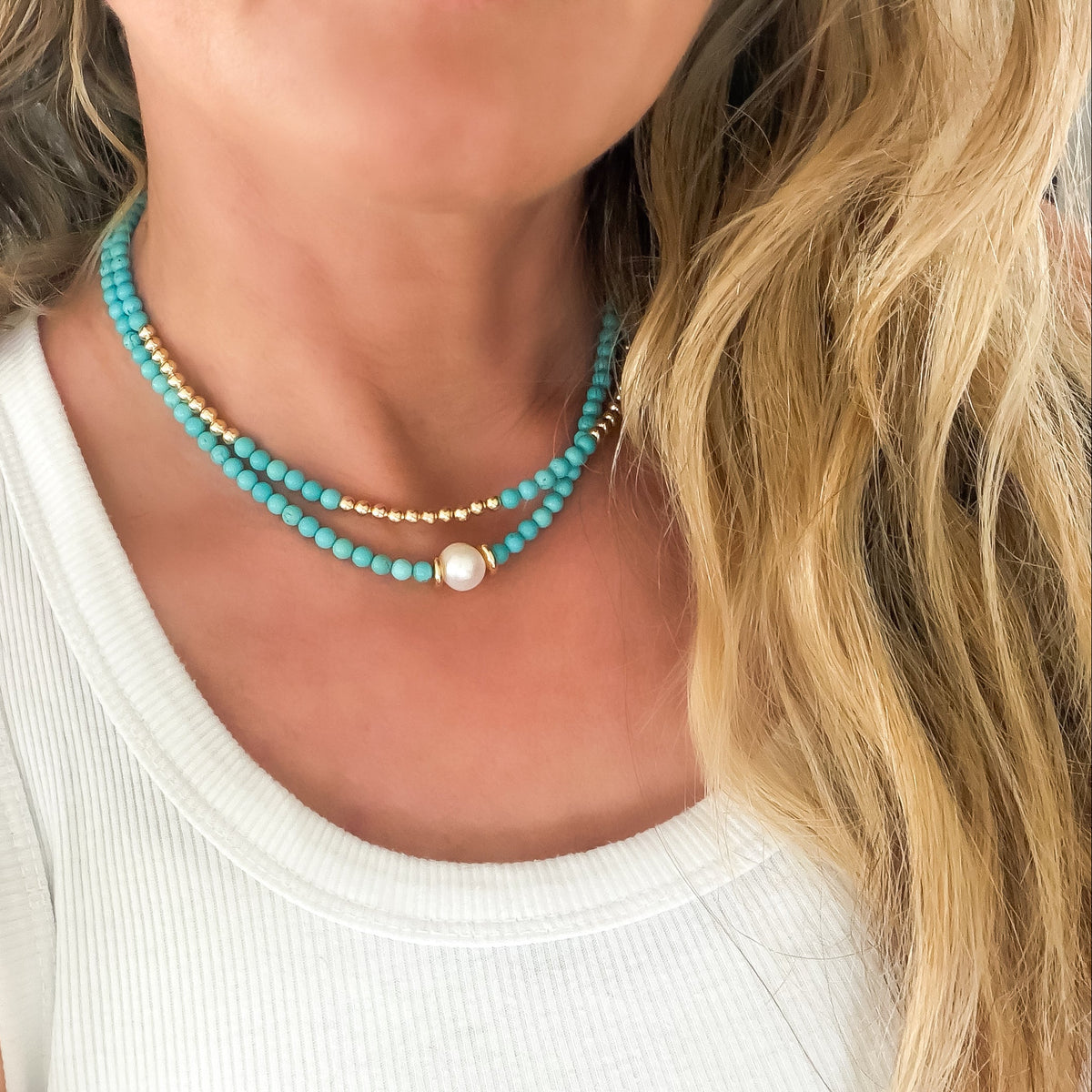Close-up of a woman wearing a turquoise beaded necklace with a pearl accent.