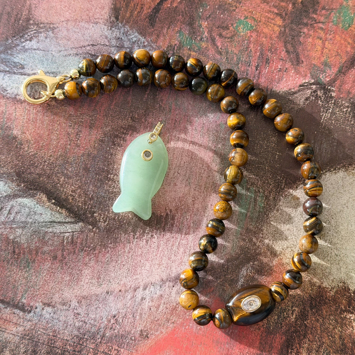 Necklace with tiger's eye beads and a jade fish pendant on a textured surface
